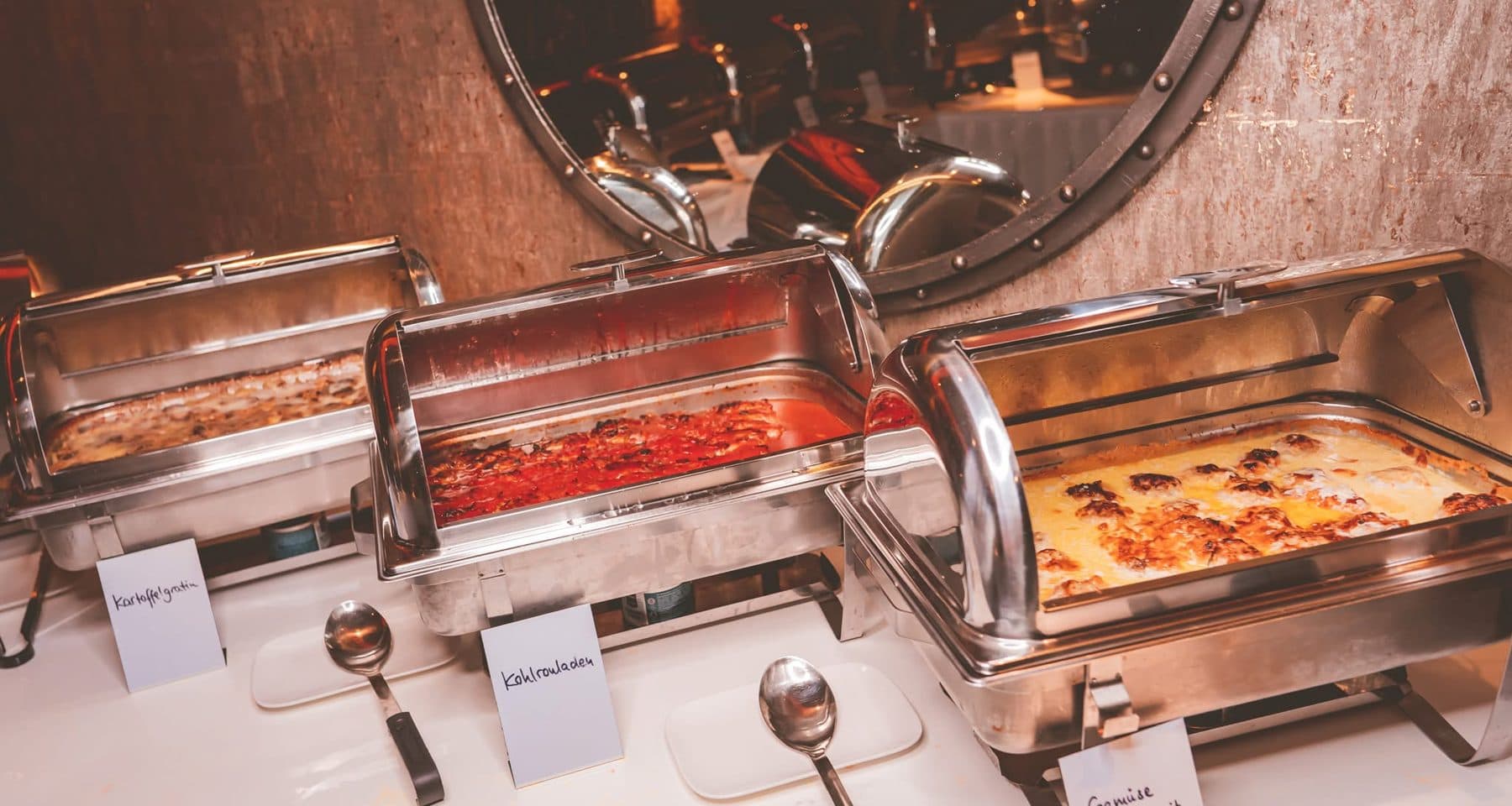 Warme Gerichte in Chafing Dishes am Buffet: Kartoffelgratin, Kohlrouladen und gefülltes Gemüse