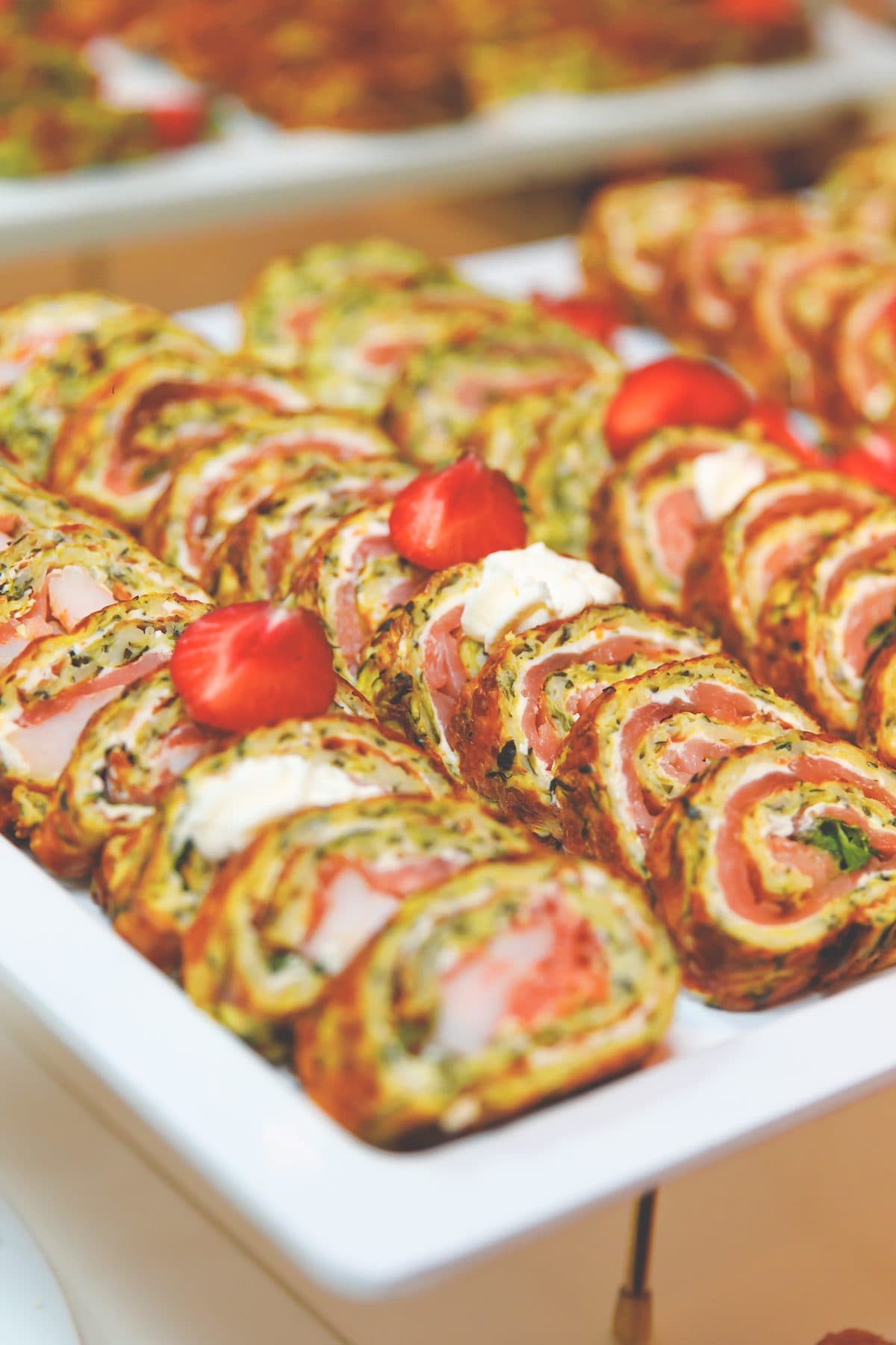 Lachs-Spinat-Röllchen mit Kirschtomaten, angerichtet auf einer weißen Platte am Buffet